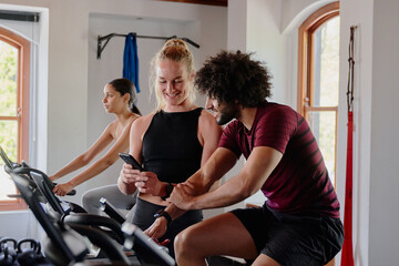 Group of young multiracial friends on exercise bike with mobile phone at the gym