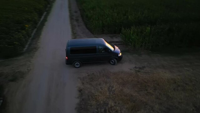 Aerial shot of Grey minivan driving on the green corn field rural road