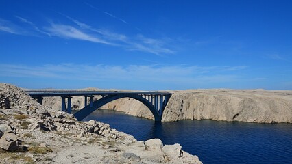 Pag Island Bridge viewed from southeastern side during sunny august summer day, blue skies with some wind blown clouds.