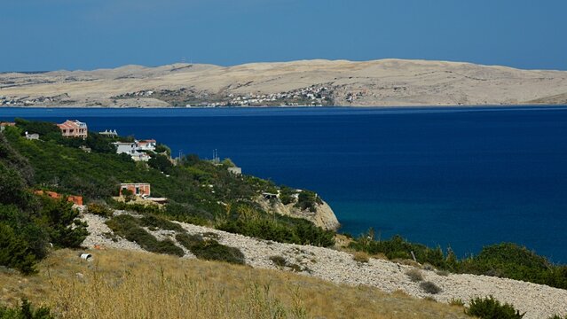 Arid foliage, rocks, settlements and appartments on shoreline of Pag island, Croatia, near Sv. Marko and beach Sv. Maria, during summer holiday season, august 2022.