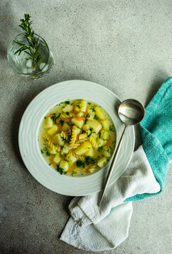 Overhead view of a bowl of healthy vegetable and pasta soup with a glass of rosemary water