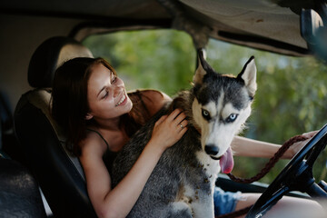 A woman rides in a car with her husky dog ​​and smiles while traveling by car to nature in the forest in summer. Lifestyle in the happiness of the way by car with a dog