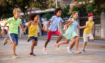 Happy tween friends having fun together on summer city street, running holding hands..