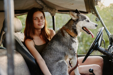 A woman sits in a car with her husky dog ​​and smiles while traveling to nature in the forest in summer. Lifestyle on the road by car with a dog