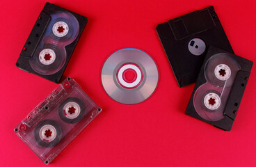 Black floppy disk, audio cassettes, and small disc on a pink background