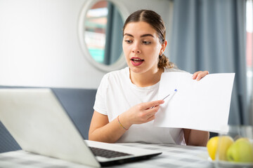 Young woman studying via internet using laptop while sitting at table at home