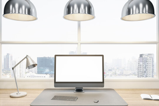 Close up of empty white computer display on wooden office desk top with objects, lamp and supplies on panoramic window and city view background. Mock up, 3D Rendering.