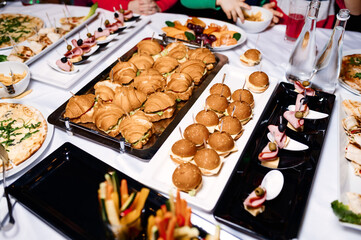 a lot of different food on the buffet, burgers, canapes, croissants and vegetables