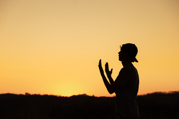 Silhouette of a man praying and thanking God with the sunset sky in the background. Receiving God's blessing.