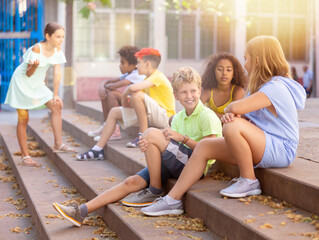 Children talking together while sitting on stairs outdoors. Youngsters chatting during summer day.