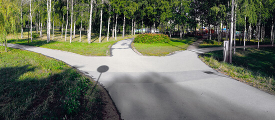 A wide asphalt track in the park diverges in three directions. Morning summer conceptual landscape