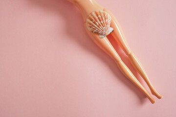 doll body and seashell on pink background