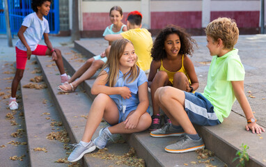 Happy tweenagers friends spending time together in city streets during summer vacations, sitting on steps and chatting ..