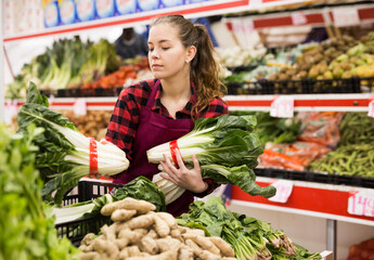 Young positive female seller displaying assortment of lettuce at supermarket