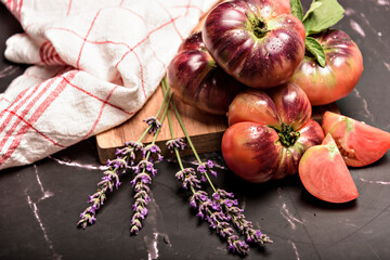Tiger tomato on a cutting board with basil leaves on wooden background. Fresh tomato wased for cooking. Tomato with droplets of water.