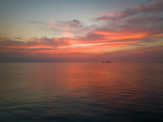 Sunrise reflects off clouds and calm ocean waters with small island in background