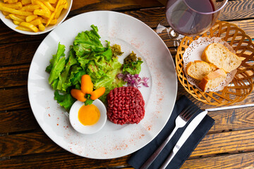 Popular cold appetizer of French cuisine is beef tartare made from raw meat, served with egg yolk, chopped onion, lettuce ..leaves and drizzled with soy sauce