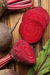 Cut and whole raw beets on wooden table, closeup