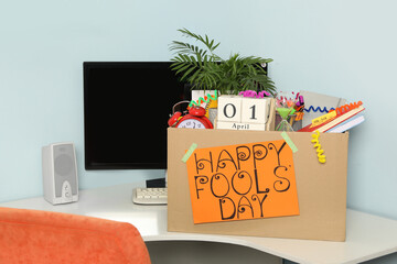 Box with different items and words Happy Fool's Day at workplace in office
