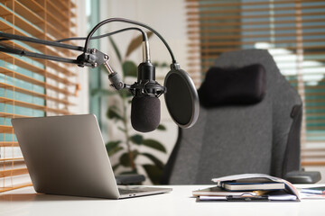 Sound recording and broadcasting equipment with microphone, laptop and headphones on wooden table in the home studio. Podcasting, broadcasting concept.