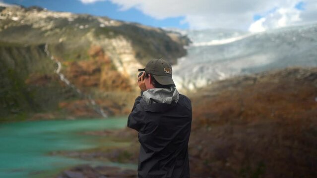 Young caucasian male photographer taking photos of epic mountain, glacier lake landscape, british columbia