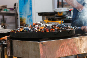Defocus seafood at cooking festival outdoor. Seafood paella. Chef grilling sausages in park...