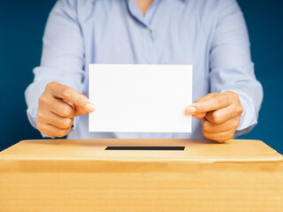 Hand voter holding ballot paper putting into the voting box at place election with a blue background