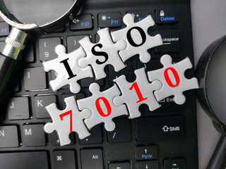 Top view puzzle and magnifying glass with the word ISO 7010 on wireless keyboard. Business concept.
