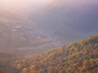 Autumn forest on high mountain over blurry village background.