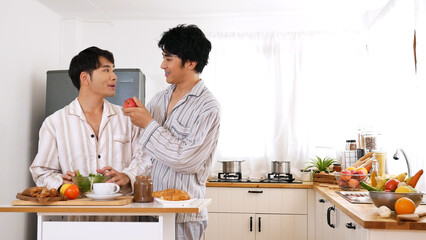 Happy gay couple enjoy breakfast in kitchen drinking coffee. Two best friends LGBTQ relation partner home cooking. Happiness romance homosexual marriage lifestyle. Two men together love friendship.