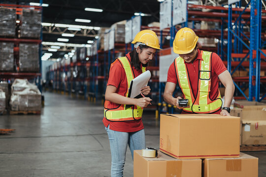 Warehouse Workers scanning barcode stock products in Logistic center. Asian workers team wearing hard hat and safety vests to talking about shipment in storehouse, Working in Distribution Center.