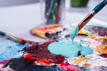 Fototapeta premium High quality photography. Palette full of paint with a brush taking it. Blue paint in a color palette. Artist materials working with acrylic paints.