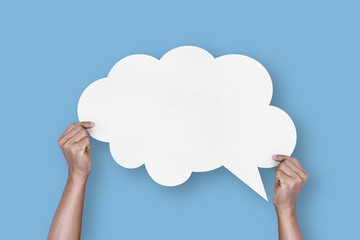 hand holding white paper cloud shape speech bubble balloon isolated on light blue background.