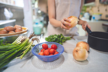 Young adult asian woman hand holding onion cooking in kitchen on day