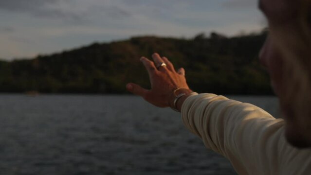 POV of a man's hand reaching out to a tropical island while sailing a boat in the ocean