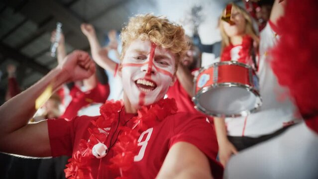 Stadium Sport Event: Selfie Portrait of Man with Painted Face Holding and Shooting Himself on Smartphone, Cheers for Red Team to Win, Screaming, Celebrating Championship Victory with Crowd