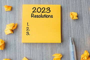 2023 RESOLUTIONS word on yellow note with pen and crumbled paper on wooden table background. New...