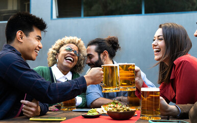 Cheers. Multiracial group of happy and smiling friends toast with beer and laugh together in a bar outdoors.