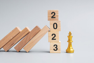 wooden Dominoes falling against 2023 stop blocks with golden Chess King figure. Business, Risk...
