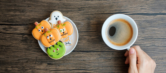 hand holding coffee cup during eating funny Halloween Cookies. Happy Halloween day, Trick or Threat, Hello October, fall autumn, Traditional, party and holiday concept