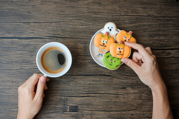 hand holding coffee cup during eating funny Halloween Cookies. Happy Halloween day, Trick or...
