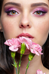 Closeup portrait of female face with pink beauty makeup and carnation flowers near lips.