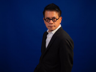 Portrait of smart middle-aged asian confident successful businessman wearing suit standing on blue background in studio, looking attractive and positive professional leadership