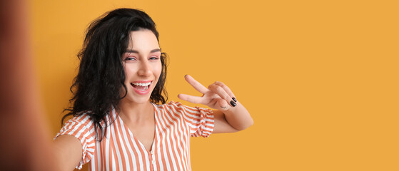Beautiful young woman taking selfie on orange background with space for text