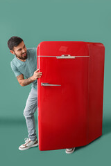 Cool tattooed young man getting out of red fridge on green background