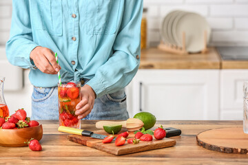 Woman with glass of tasty cold strawberry lemonade in kitchen