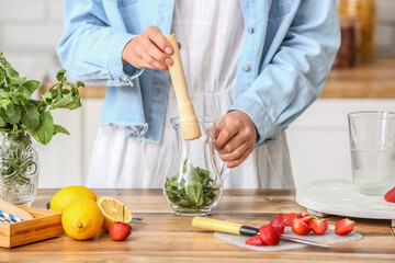 Woman preparing tasty strawberry lemonade on kitchen counter