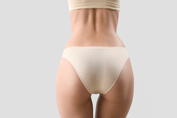 Slim young woman in underwear on light background, back view