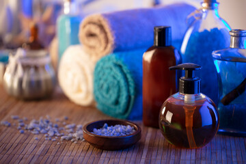 Spa and wellness concept. Bottles with bath and spa cosmetics, rolled up towels, bath salts and...