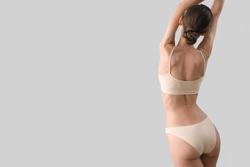 Slim young woman in underwear on light background, back view